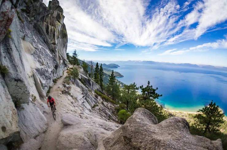 Mountain biker riding along a dirt trail with panoramic views of Lake Tahoe and the Sierra Nevada.