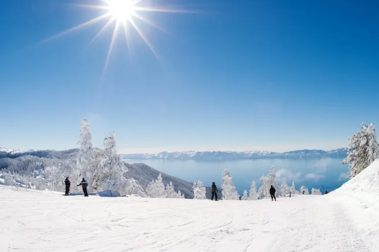 Skier descending a groomed slope with Lake Tahoe and Sierra Nevada mountains in the background.
